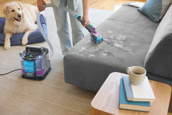 Woman cleans dog hair off couch with Shark cleaner. 