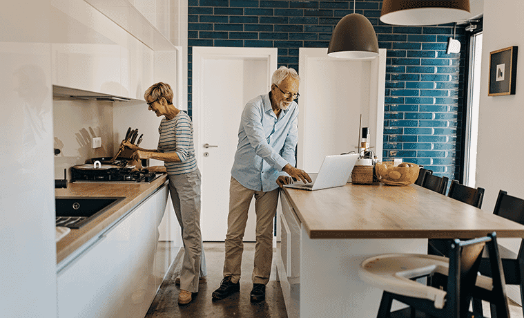Senior couple cook together in their kitchen with white highgloss cabinetry stone benches and highend kitchen appliances
