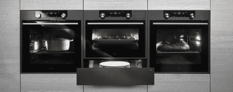 Three black builtin wall ovens on grey cabinets 