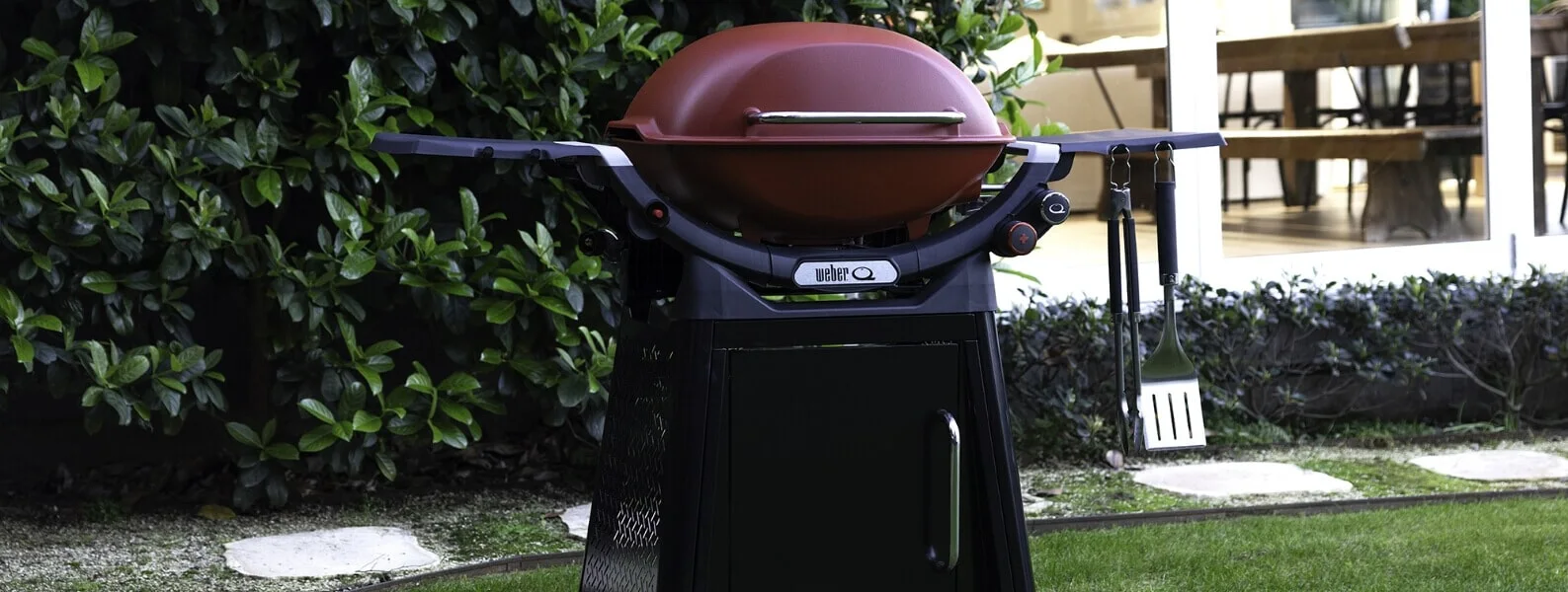 A black Weber Family Q BBQ stands next to an outdoor kitchen in a backyard