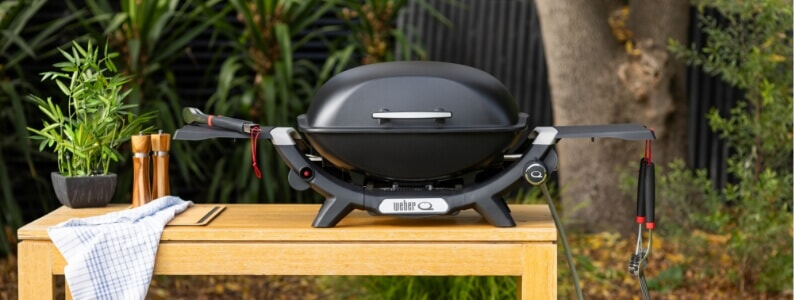 A black Weber Q BBQ sits on a table in a backyard