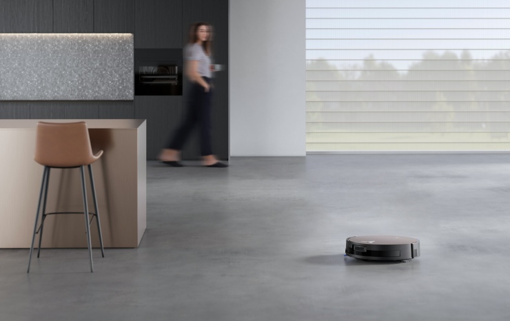 ECOVACS robot vacuum on concrete in womans kitchen. 