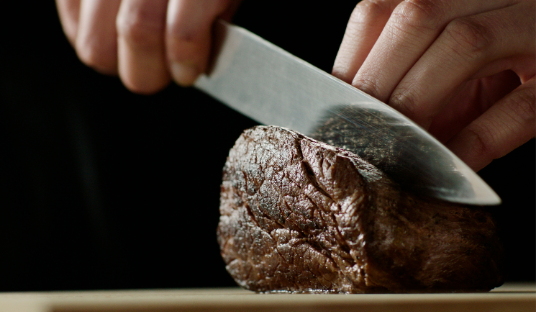 Close up image of a knife carving through perfectly cooked meat