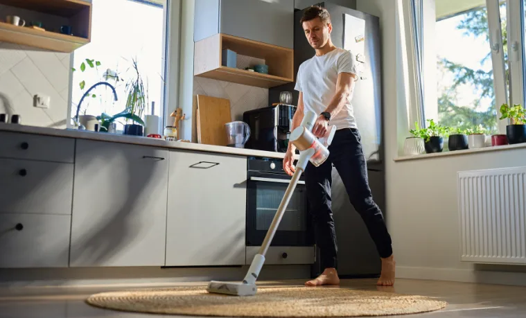 Man cleaning his kitchen with a stick vacuum.