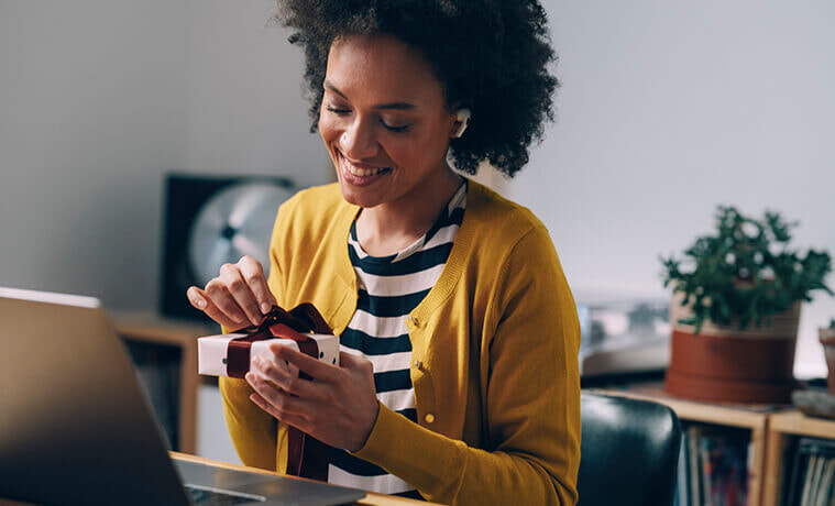 A woman opens up a small Christmas gift in front of her laptop