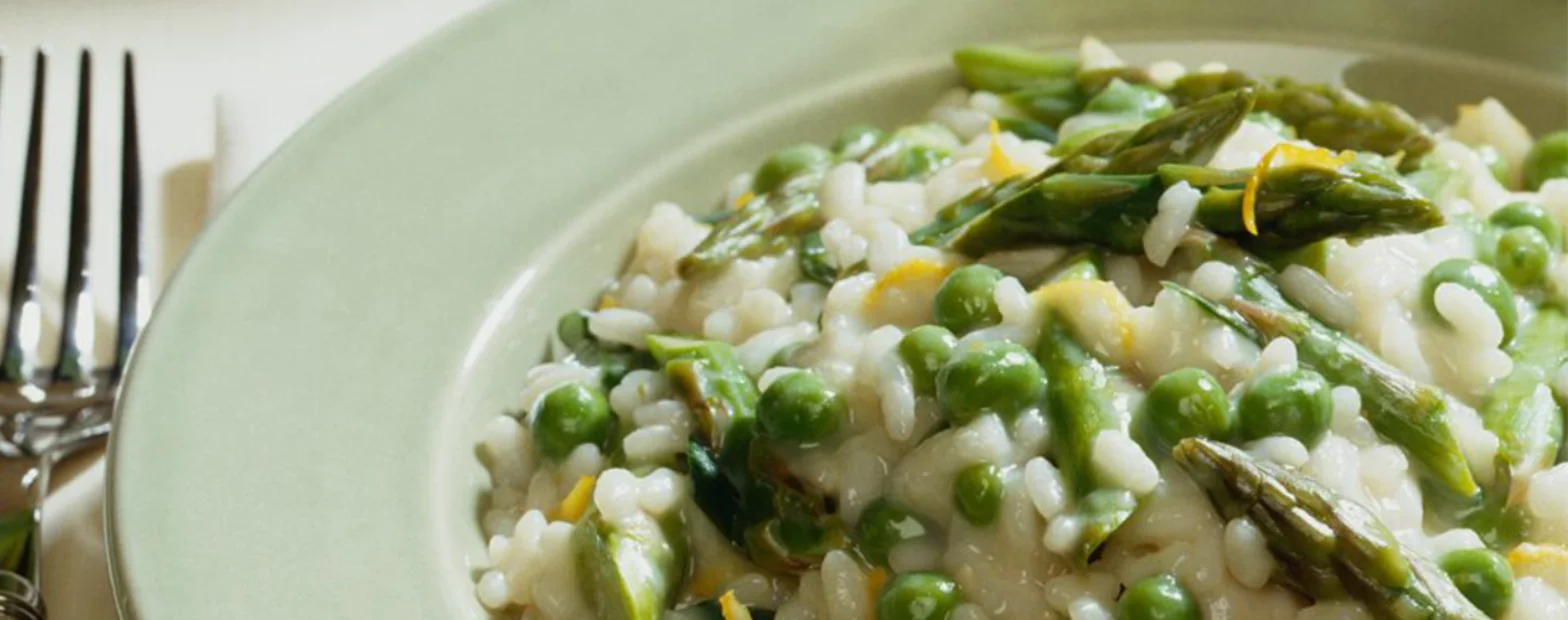 Creamy risotto with green peas, asparagus and lemon zest in a pale green bowl.