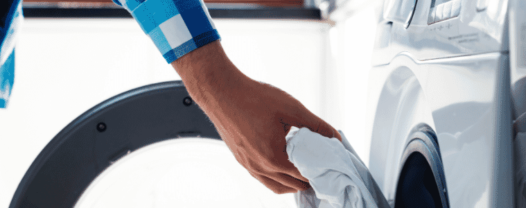 A mans arm reaches in to remove clothing from a dryer