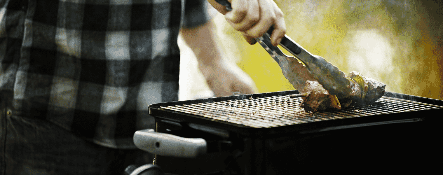 Man holding tongs barbecues kebabs on a grill