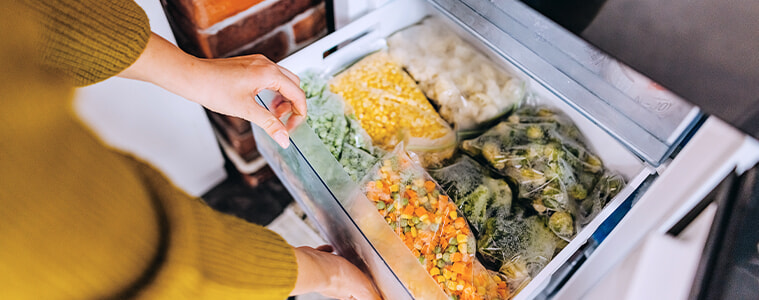 Woman putting a container with frozen mixed vegetables into the drawer of her fridgefreezer 