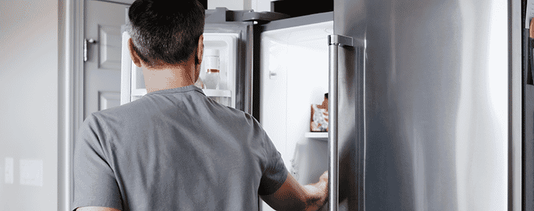 Man in a grey shirt opening the freezer door of a sidebyside fridge to look for ingredients