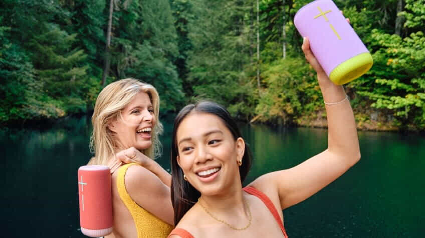 Image of two women smiling at a lake while both holding an Ultimate Ears Everboom Bluetooth Speaker