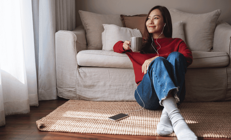a woman listening to music on their iPhone and drinking coffee