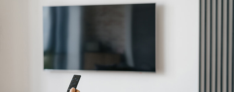 Man holds the remote up to a big screen TV mounted on a living room wall