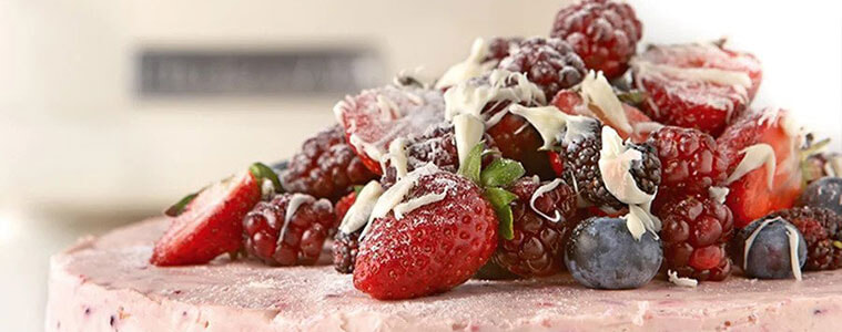 Close up image of a pink berry cheesecake with a mound of fresh fruit berries and white chocolate shavings