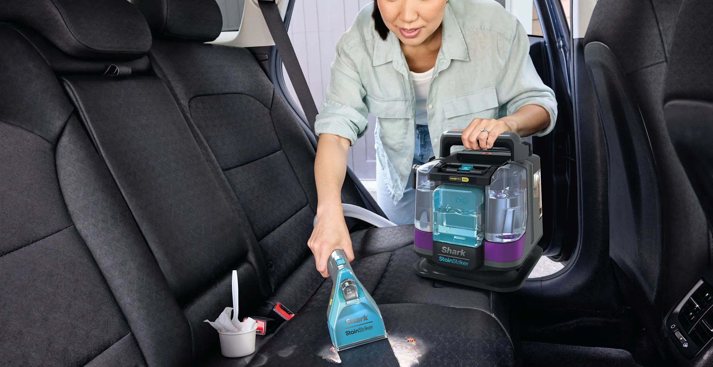 Image of a woman using the Shark StainStriker HairPro Portable Carpet Upholstery Cleaner to clean the inside of a car