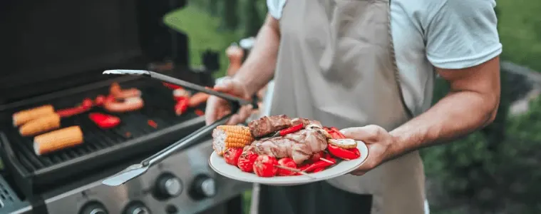 A man standing infront of a bbq with a plate of meats