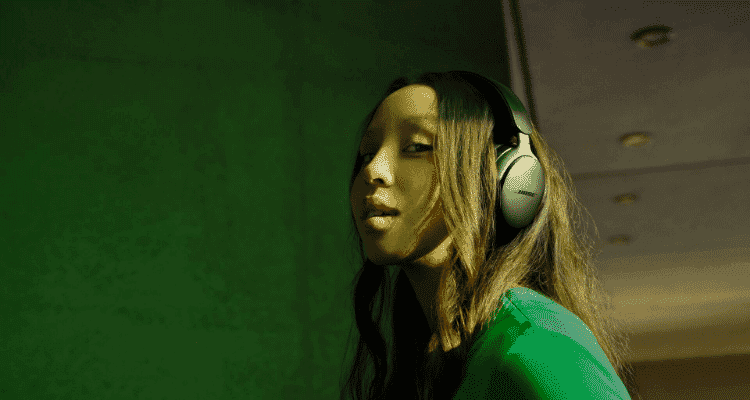 A woman wearing the Bose Quietcomfort Ultra Headphones infront of a green background