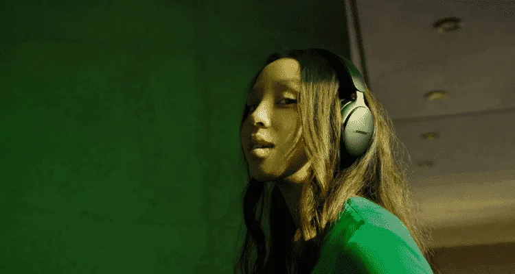A woman wearing the Bose Quietcomfort Ultra Headphones infront of a green background