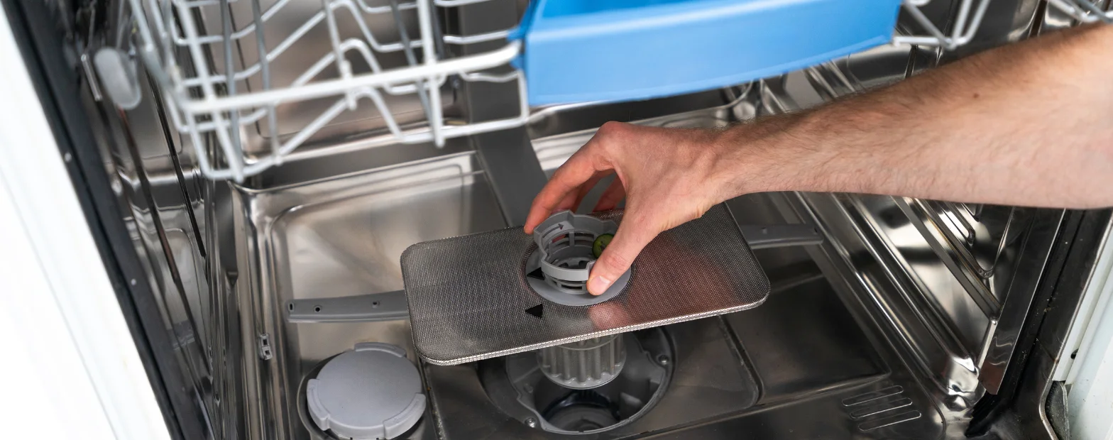 A hand removing the filter from a dishwasher