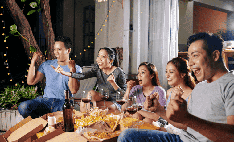 A group of friends watch a movie outdoors on a projector