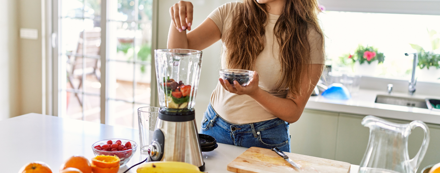 Image of a woman pouring blueberries into a blender filled with fruit and vegetables