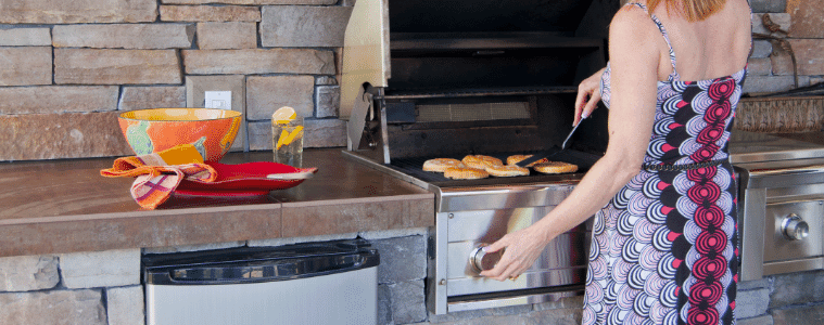 Woman cooks on her builtin BBQ in her outdoor kitchen