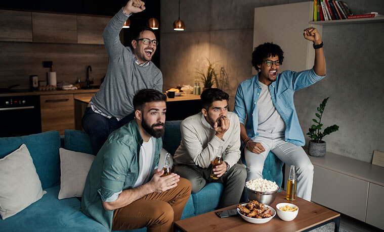 A group of male sports fans share a living room couch to watch a game together eyes on the screen and cheering