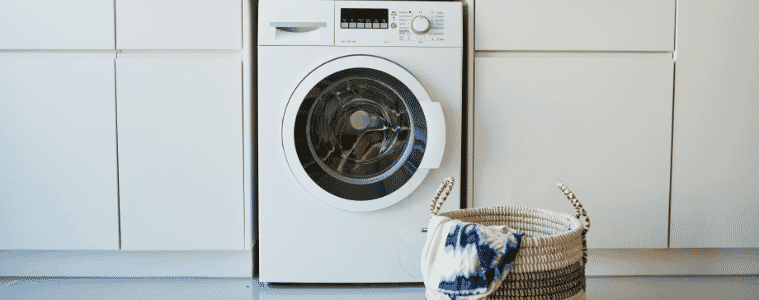 A white washing machine in a white laundry with a basket of washing in front of it
