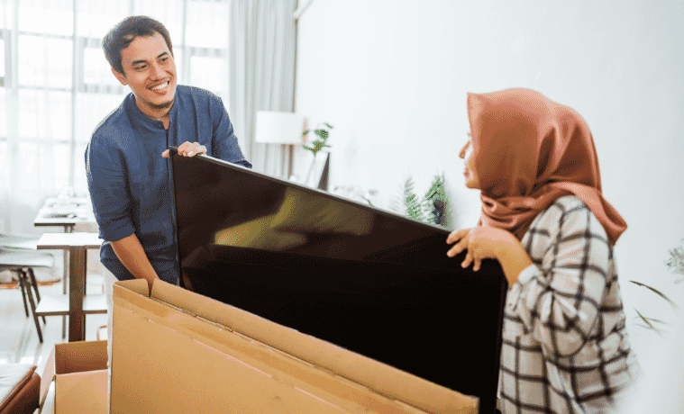 A man and a woman unpacking their new TV into their home 