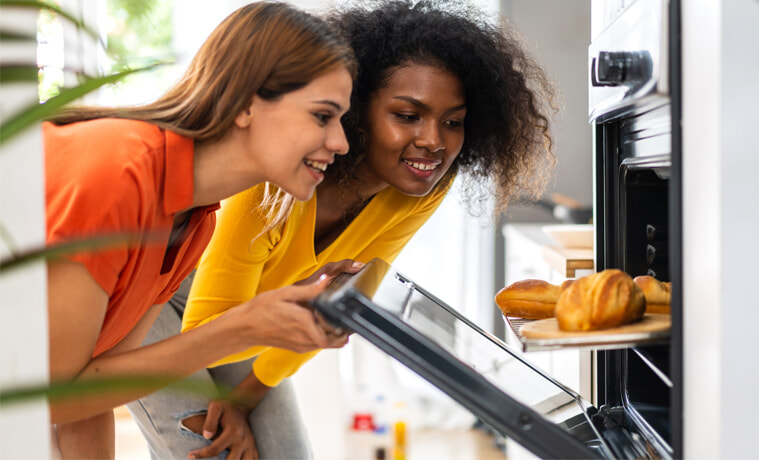 Two female friends open a steam oven to check their baking