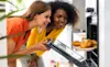 Two female friends open a steam oven to check their baking