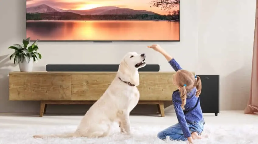 A little girl plays with a golden retriever in her living room in front of a TCL soundbar