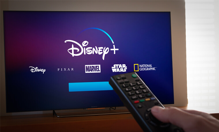 A person uses a remote to navigate to Disney Plus on their TV