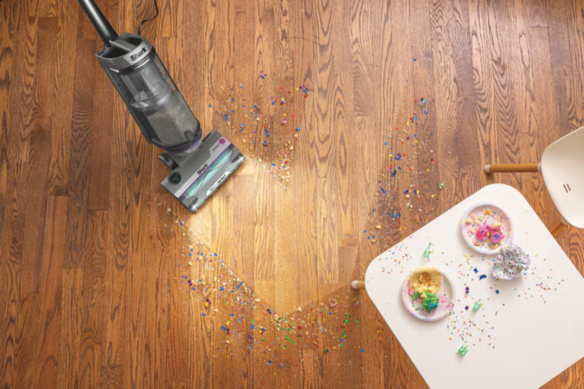 Shark upright vacuum vacuuming up confetti off floor. 