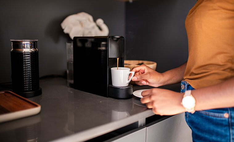A close up view of a woman using her capsule coffee machine to fill her coffee cup for a morning brew in her kitchen