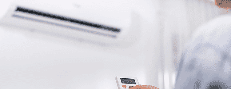 A woman holding the remote control for an air conditioner on a white wall