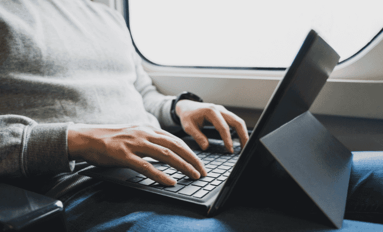 A man types on a laptop while riding the train
