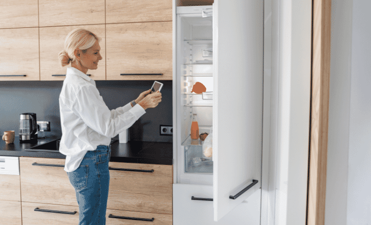a women looking at her iPad whilst getting food out of her smart fridge 