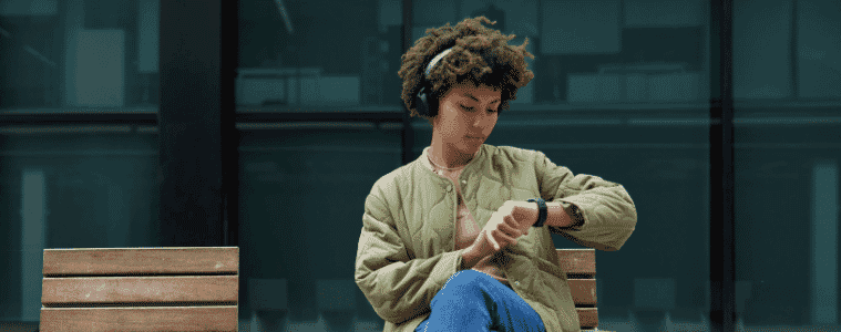 Woman relaxes on a seat whilst using her noise cancelling headphones and smartwatch