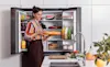 A woman stands in front of the open Samsung 648L French Door Fridge holding a platter 