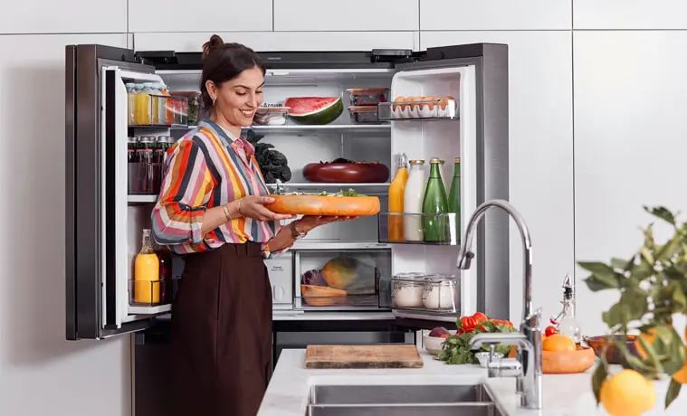 A woman stands in front of the open Samsung 648L French Door Fridge holding a platter 