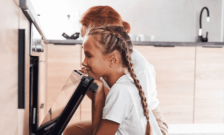 A young girl opening and looking into an oven in a kitchen