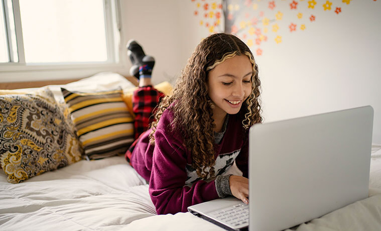 A teenage girl lie on her bed while using her laptop
