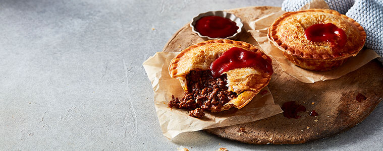 Crispy golden homemade meat pies on a bench with a white cloth and a small dish of tomato sauce