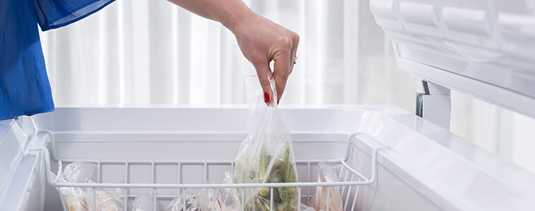 A man bends down to remove an item from the open freezer drawer at the base of his fridge