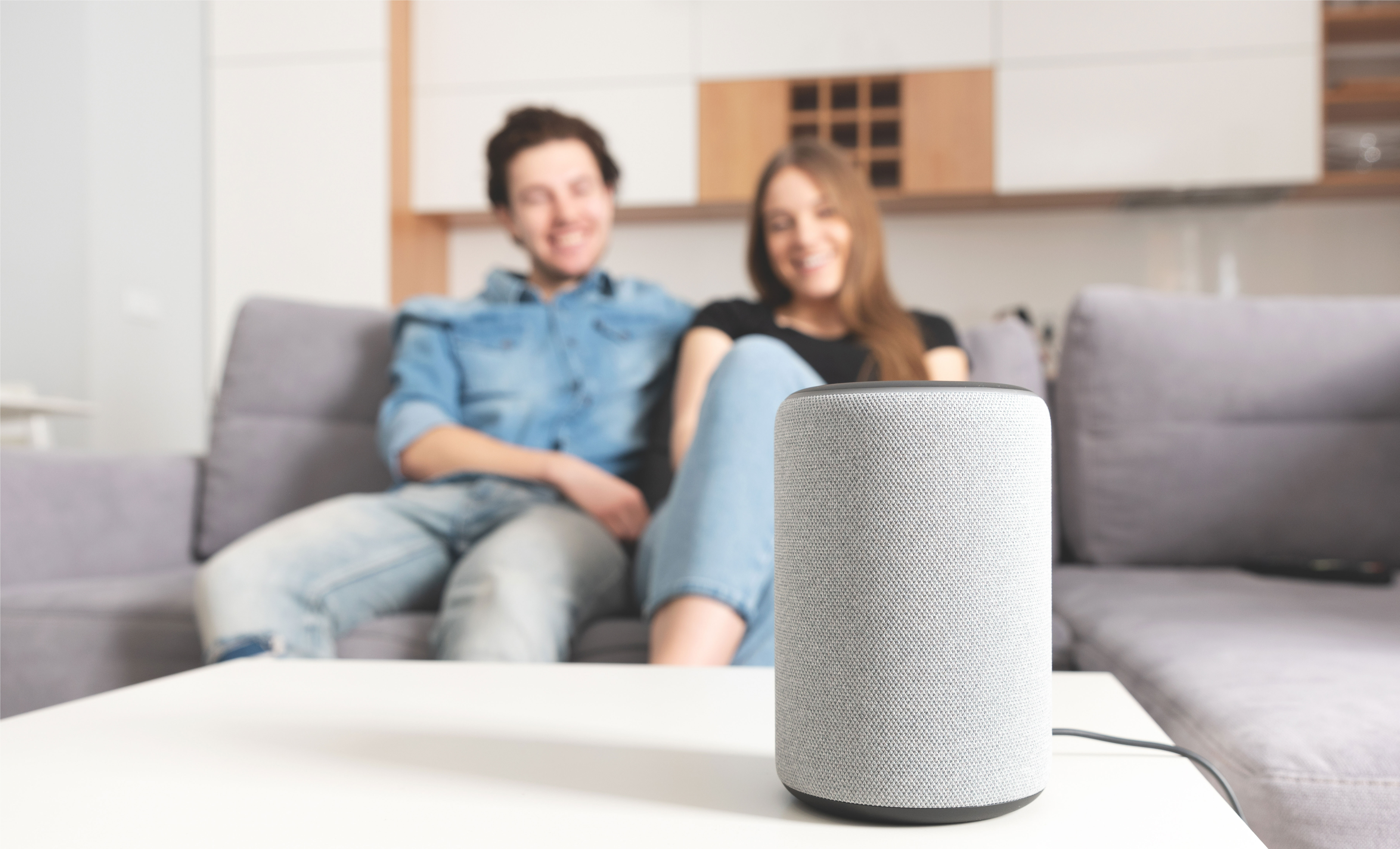 A couple sit on their couch and look at their smart home device