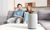 A couple sit on their couch and look at their smart home device