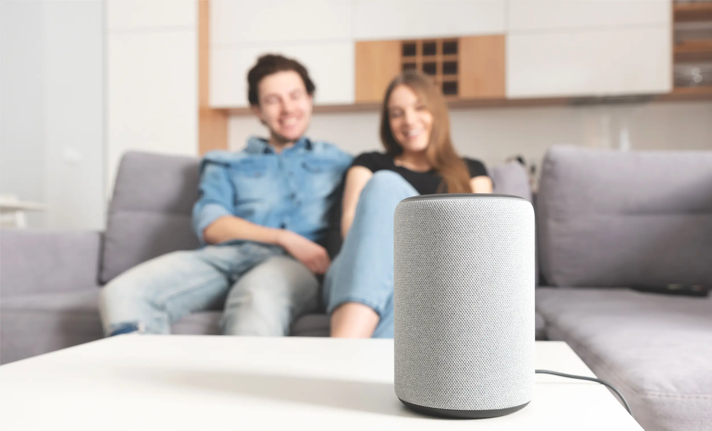 A couple sit on their couch and look at their smart home device