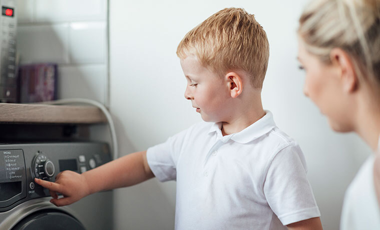 A mum shows her son how to use the washing machine in their laundry