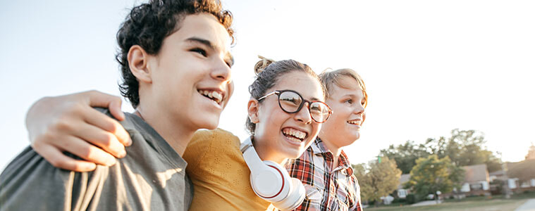 Three teenagers one with headphones walk and laugh together